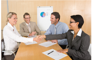 four people at a conference table with two shaking hands